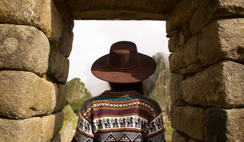A girl in a hat looking out of a window in the ruins at Machu Picchu